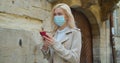 Young woman in protective mask using smartphone in the street of old city. Worried girl searching news about Covid-19