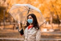 Young woman in protective mask walking with umbrella at park on autumn day Royalty Free Stock Photo