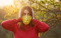 A young woman in a protective medical mask covers her ears from false news with her hands. Massive