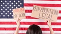 Young woman protester holds cardboard with Keep Abortion Legal and Bans Of My Body signs against USA flag on background. Girl Royalty Free Stock Photo