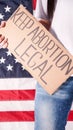 Young woman protester holds cardboard with Keep Abortion Legal sign against USA flag on background. Girl protesting against anti-