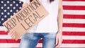 Young woman protester holds cardboard with Keep Abortion Legal sign against USA flag on background. Girl protesting against anti-