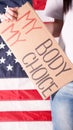 Young woman protester holds cardboard with My Body My Choice sign against USA flag on background. Girl protesting against anti-