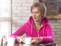 A young woman in a purple hoodie sits in a cafe and drinks coffee from a white cup