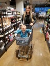 Beautiful young woman pushing shopping cart in store between shelves with food and drinks while her little son sitting Royalty Free Stock Photo