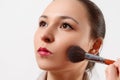 A young woman puts makeup on her face with a brush. on white background Royalty Free Stock Photo