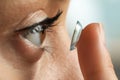 Young woman putting contact lens in her eye on blurred background, closeup Royalty Free Stock Photo