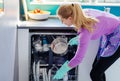 Young woman putting dirty dishes to dishwasher