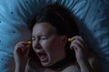 Young woman putting earplugs into her ears for the noise reduction before sleep, insomnia Royalty Free Stock Photo