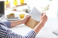 Young woman putting letter into envelope at table in cafe. Mail delivery