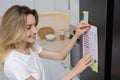 Young woman putting to do list on refrigerator in kitchen Royalty Free Stock Photo