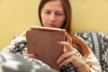 Young woman in pyjama, laying in bed, covered with duvet, working with her tablet before sleeping.