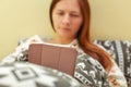 Young woman in pyjama, laying in bed, covered with duvet, workin Royalty Free Stock Photo