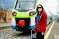 Young woman on a railway station. A girl waiting for a train on a platform. Female tourist with a luggage suitcase ready to travel Royalty Free Stock Photo