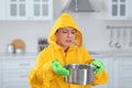 Young woman in raincoat collecting leaking water from ceiling at home. Time to call repair service Royalty Free Stock Photo