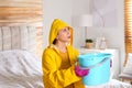 Young woman in raincoat collecting leaking water from ceiling at home. Time to call roof repair service Royalty Free Stock Photo