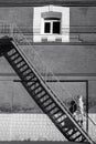 A young woman in a raincoat and dark glasses, with a suitcase in her hands, climbs the fire escape against the background of a bri Royalty Free Stock Photo