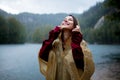 Woman in raincoat near lake in rainy day.