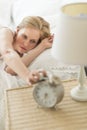 Young Woman Reaching For Alarm Clock While Lying On Bed