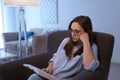 Young woman reading book on armchair at home in evening Royalty Free Stock Photo