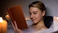 Young woman reading book in bath with foam and candles, evening relaxation Royalty Free Stock Photo