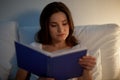 Young woman reading book in bed at night home Royalty Free Stock Photo