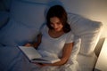 Young woman reading book in bed at night home Royalty Free Stock Photo