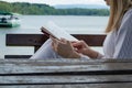 Woman with book on legs lap sitting on bench and reading near lake in nature. Relaxation and resting concept Royalty Free Stock Photo
