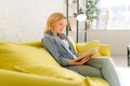Young woman reading a book on cozy yellow couch Royalty Free Stock Photo