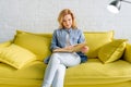 Young woman reading a book on cozy yellow couch Royalty Free Stock Photo