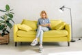 Young woman reading a book on cozy yellow couch Royalty Free Stock Photo