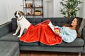 Young woman reading book and drinking coffee lying on sofa with dog at home Royalty Free Stock Photo