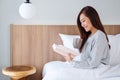 A young woman reading book and drinking hot coffee in a white cozy bed at home Royalty Free Stock Photo