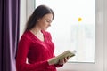 Young woman in reading book, girl stands near window with yellow fallen leaf Royalty Free Stock Photo