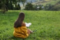 Young woman reading book on green meadow, back view Royalty Free Stock Photo