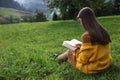 Young woman reading book on green meadow, back view Royalty Free Stock Photo