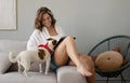 Young woman reading book and her cute dog on sofa at home. Lovely pet.