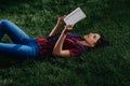 Young woman reading book while lying on green grass outdoors Royalty Free Stock Photo