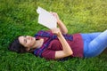 Young woman reading book while lying on green grass outdoors Royalty Free Stock Photo