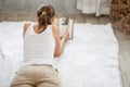 Young woman reading book while lying on White furry carpet in living room at home in quarantine