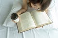 Young woman reading book with morning coffee cup in bedroom at home..Asian girl drink tea top view lying on cozy bed with pillow Royalty Free Stock Photo