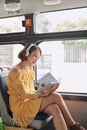 Young woman reading book while moving in the modern tram, happy passenger at the public transport