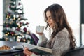 Young woman reading book near Christmas tree at home. Royalty Free Stock Photo