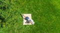 Young woman reading book in park, student girl relaxing outdoors sitting on grass with book and headphones, aerial drone view Royalty Free Stock Photo