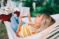 Young woman reading book, relaxing in hammock outdoors, in the backyard garden Royalty Free Stock Photo