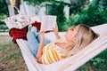 Young woman reading book, relaxing in hammock outdoors, in the backyard garden Royalty Free Stock Photo