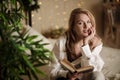 Young woman reading a book while sitting on her bed at home in the evening