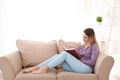 Young woman reading book on sofa at home Royalty Free Stock Photo