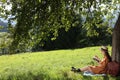 Young woman reading book under tree on meadow in mountains Royalty Free Stock Photo