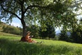 Young woman reading book under tree on meadow in mountains Royalty Free Stock Photo